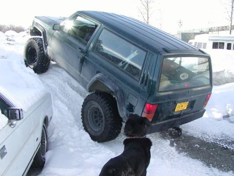 1979 Ford F-150 - A dark green SUV navigates a snowy path, with a white car partially visible on the left.