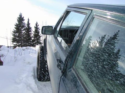 1979 Ford F-150 - A dark green SUV with large tires is parked in a snowy landscape, with pine trees visible in the background.