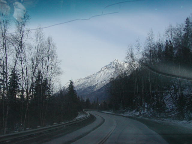 Winding road through snowy forest with snow-capped mountain in background