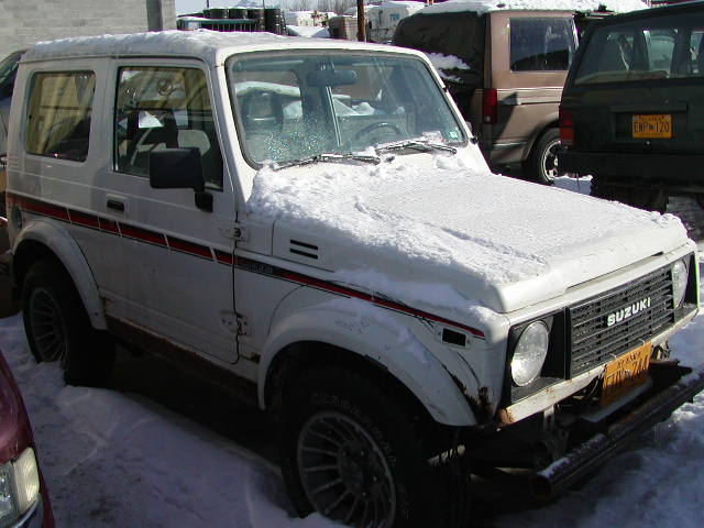 White Suzuki Samurai SUV covered in snow with yellow license plate
