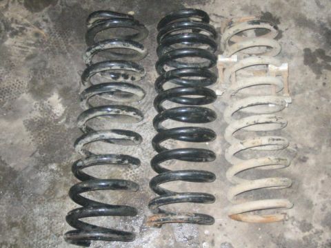 1979 Ford F-150 - Three sets of coil springs are laid out on a concrete surface, showing variations in color and condition.