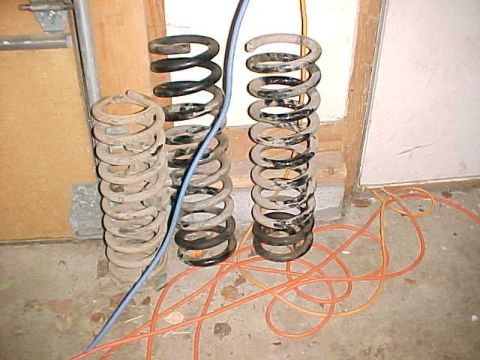 1979 Ford F-150 - Several suspension springs are visible on the floor, some appear rusty and others are black. Orange electrical cords are also present.