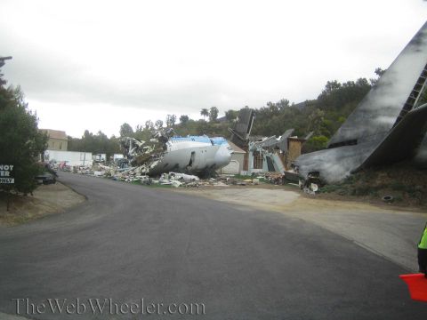 1990 Ford Bronco - staged airplane crash scene with a broken fuselage and severed tail section piled beside a road on an overcast day.