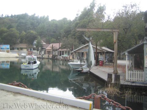 1990 Ford Bronco - studio backlot lagoon showing a small white boat and a mounted prop shark beside weathered wooden dock structures.