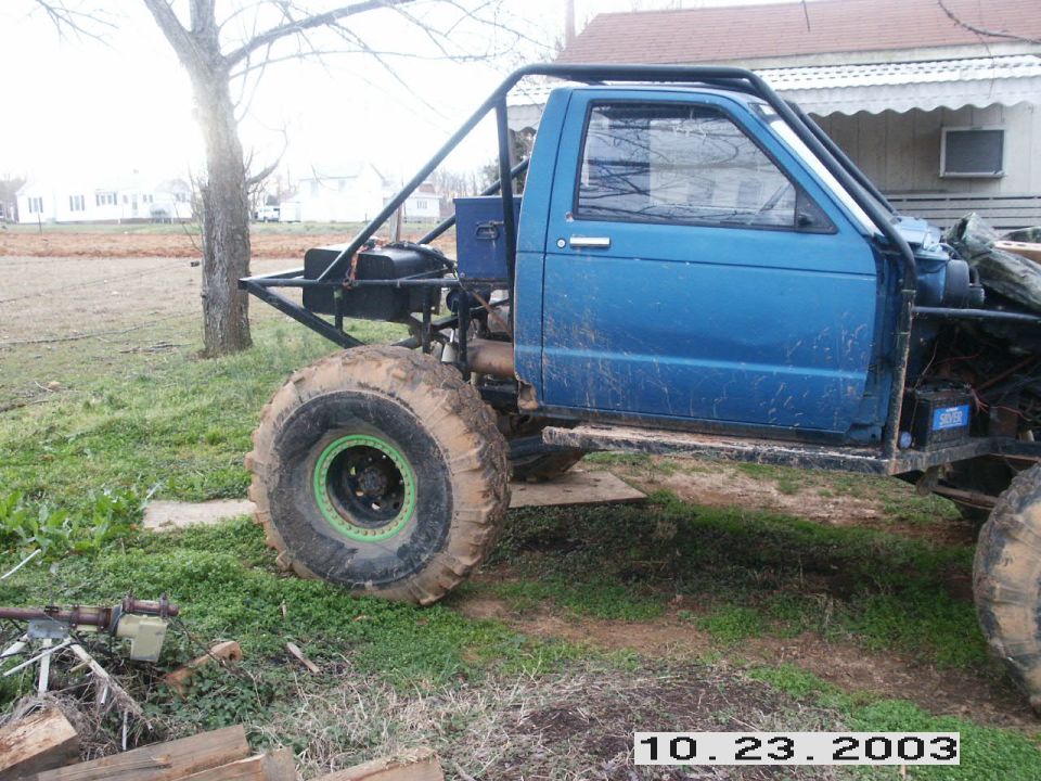 Blue custom off-road truck with large tires and a roll cage, parked on grass