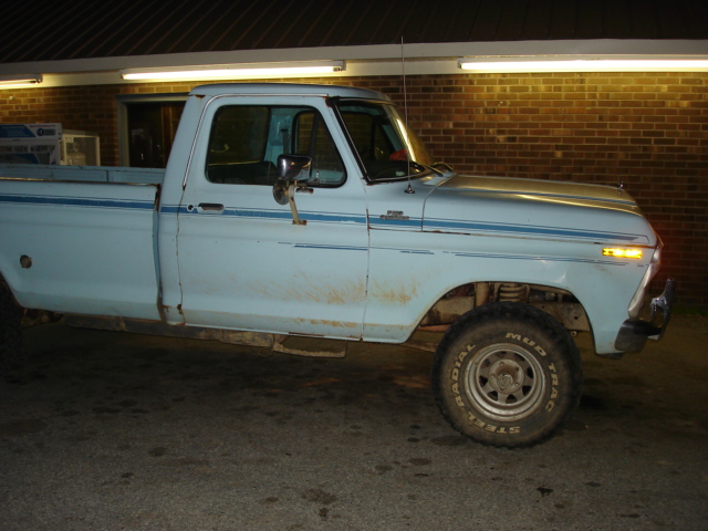 Light blue 1977 Ford F-150 pickup truck, side view, with blue trim stripes and some dirt on the body