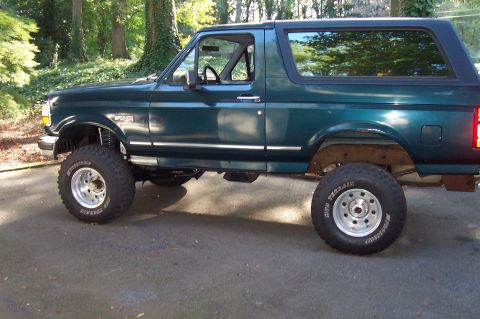1994 Ford Bronco - This lifted green Ford Bronco has a dark roof and chrome trim along the body.