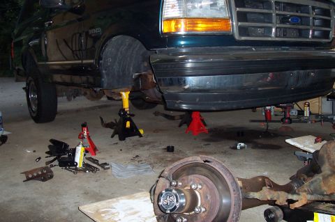 1994 Ford Bronco - A dark green 1994 Ford Bronco is raised on jack stands with its front end undergoing repairs.