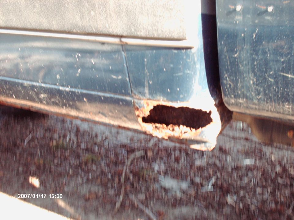 Close-up of a rusted-out rocker panel on a dark-colored truck