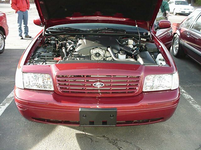 Dark red Ford Crown Victoria sedan front view with hood open showing engine bay