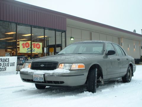 2000 Ford Crown Victoria - A 2000 Ford Crown Victoria sits in the snow, with a store's sale banner visible in the background.