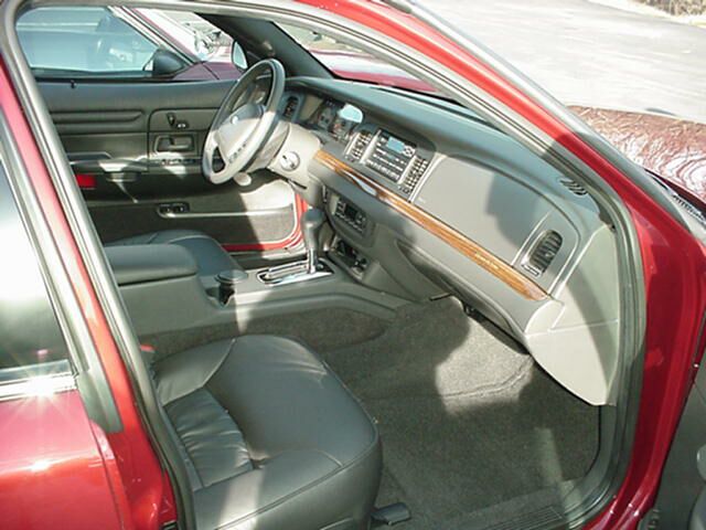 Interior of maroon sedan with gray leather seats and woodgrain dash trim, viewed from passenger door.
