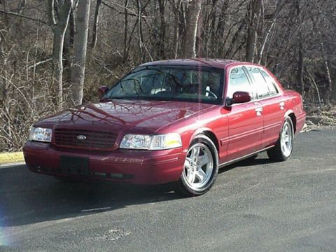 2002 Ford Crown Victoria - A red 2002 Ford Crown Victoria sedan is parked on an asphalt surface with trees in the background.