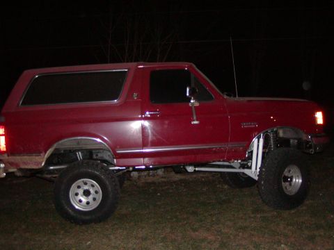 1991 Ford Bronco - This lifted red Ford Bronco is shown from the side at night, with its modified suspension clearly visible.