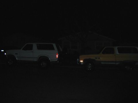 1993 Ford Bronco - Two SUVs, a white Ford Bronco and a yellow Chevrolet K5 Blazer, are parked outside a house at night.