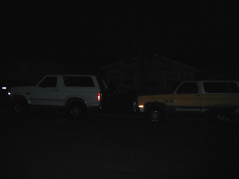 White 1992 Ford Bronco and yellow 1980s Chevrolet K5 Blazer parked side-by-side at night