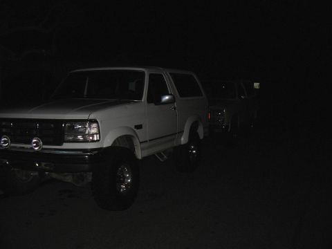 1993 Ford Bronco - Two SUVs are parked outside at night, one is white and the other is darker.