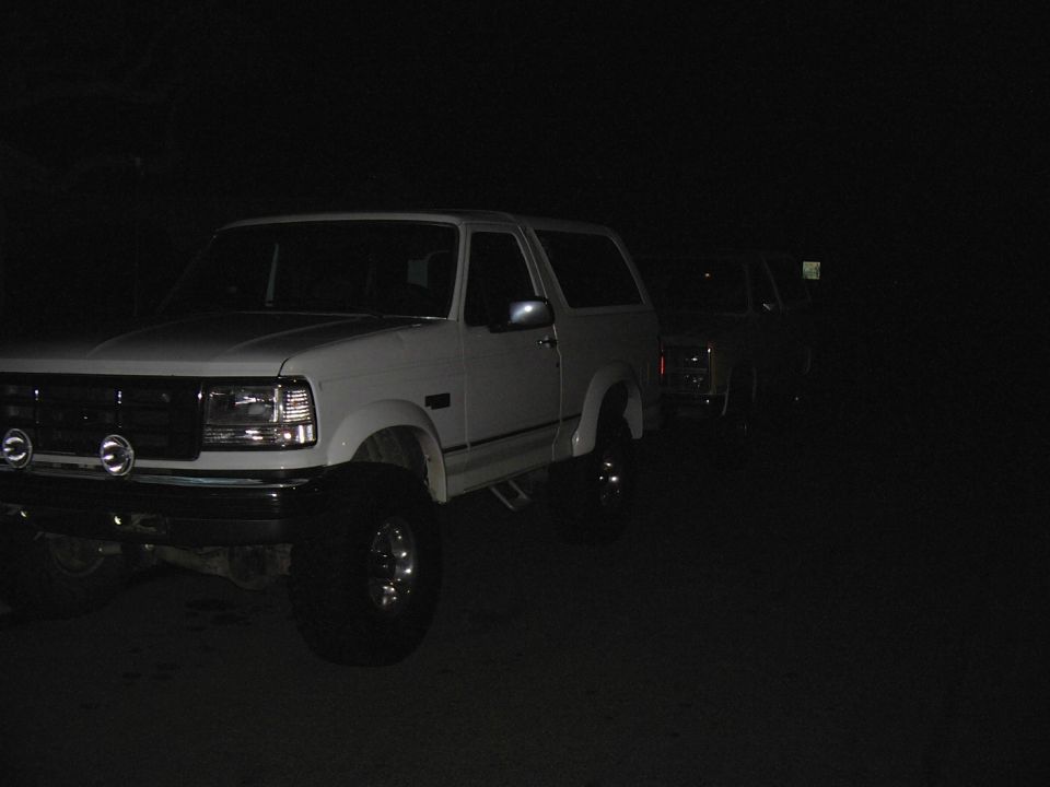 White Ford Bronco and another SUV parked at night