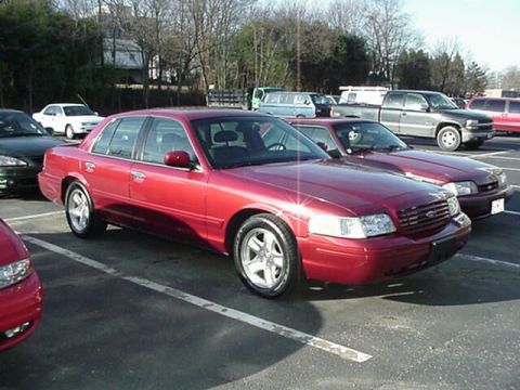 2002 Ford Crown Victoria - A red 2002 Ford Crown Victoria is parked in a lot with other vehicles visible.
