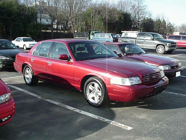 Dark red Ford Crown Victoria sedan on polished five-spoke alloys in a parking lot
