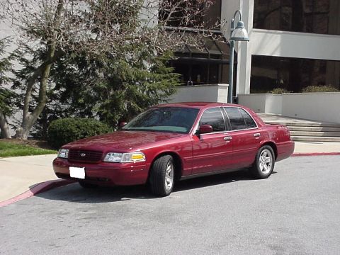 2002 Ford Crown Victoria - A red 2002 Ford Crown Victoria sedan is parked in front of a building.