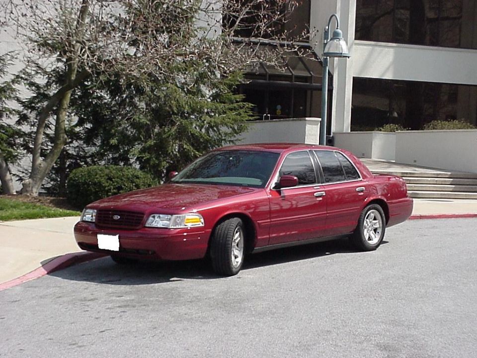 Dark red Ford Crown Victoria sedan, front three-quarter view outside an office building