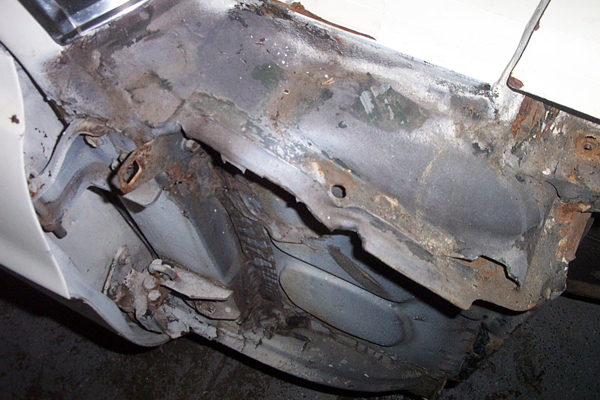 Heavily rusted car frame section with visible structural damage and missing metal