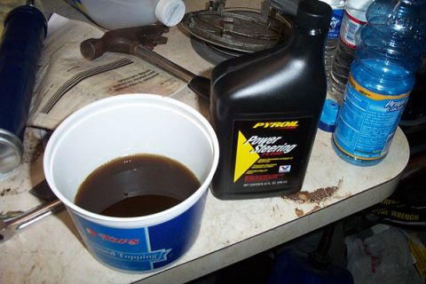 1999 Chrysler 300M - A bottle of Pysoil Power Steering fluid sits beside a bucket of used oil and a hammer on a table.
