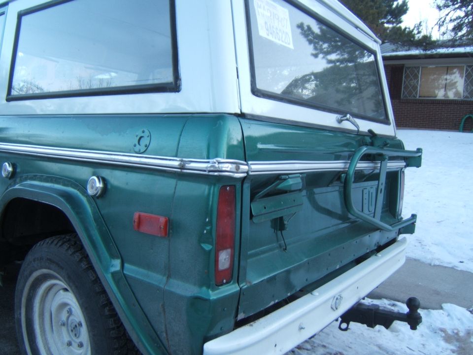 Green and white early Ford Bronco rear quarter view with spare tire carrier, parked on snow