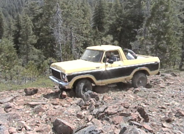 Yellow and black Ford Bronco driving over rocks in a forest