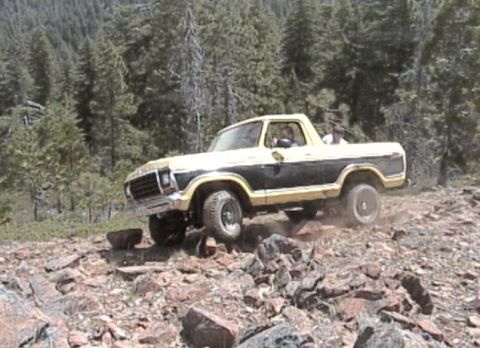 1979 Ford Bronco - A 1978 Ford Bronco navigates a challenging, rocky terrain in a forested area.