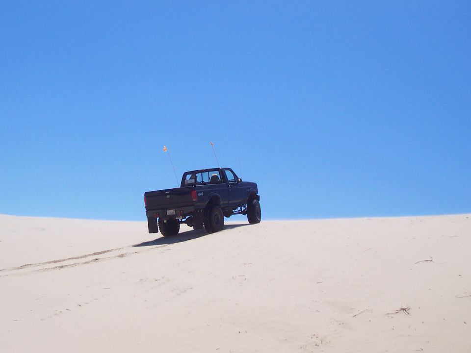 dark blue 1994 Ford F-150 driving up a sand dune with two flags on the back