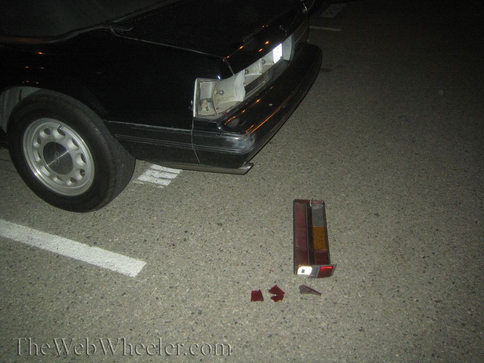 Black car rear, missing taillights with pieces on the ground. 1980s body style