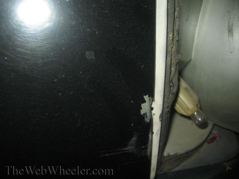 1985 Ford Mustang - Close-up view of a damaged black car door edge, revealing chipped paint and an interior light fixture.