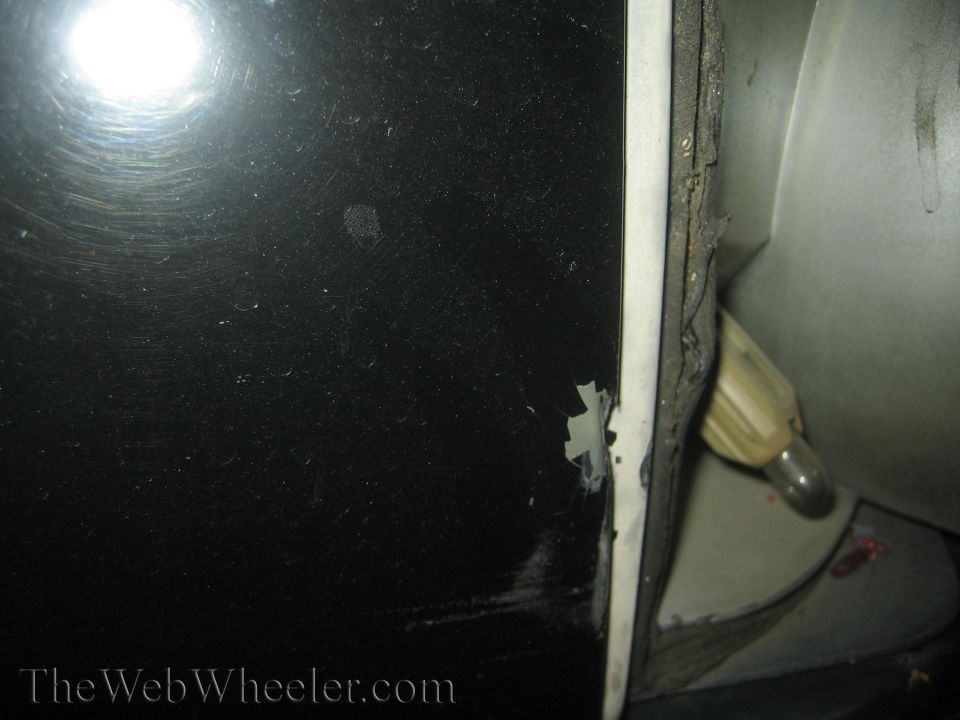 Black car door edge showing chipped paint and a light fixture inside