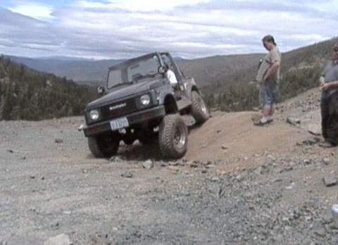 1979 Ford Bronco - A black off-road SUV navigates a steep dirt incline with two people observing.