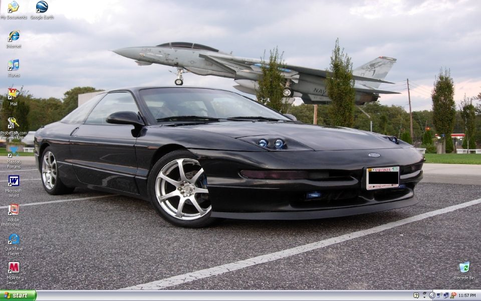 Black sports coupe parked near a fighter jet display, shown as desktop wallpaper