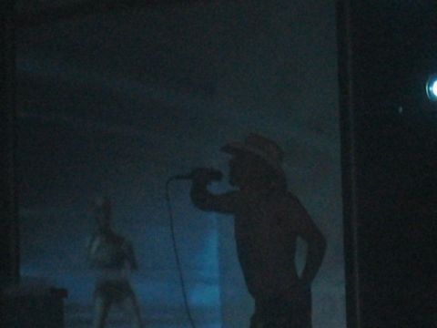 1991 Ford Bronco - A performer sings into a microphone on a dimly lit stage with another figure visible behind them.