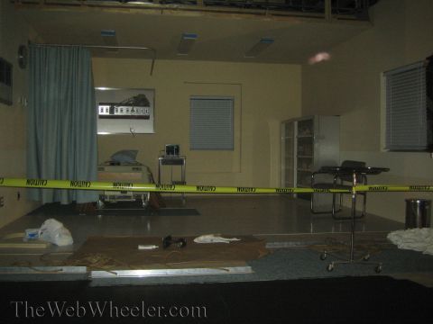1990 Ford Bronco - dimly lit interior set resembling a hospital room, cordoned with yellow caution tape and littered with debris on the floor.