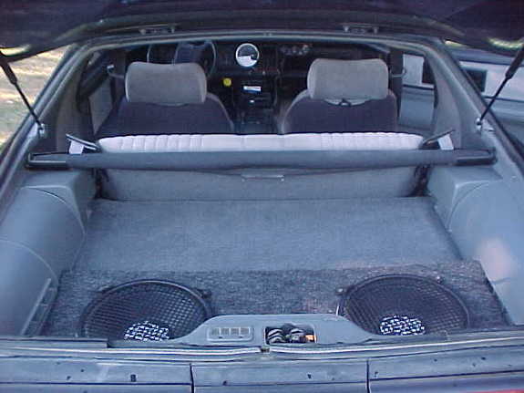 Custom carpeted rear cargo enclosure with two subwoofers seen through a hatch