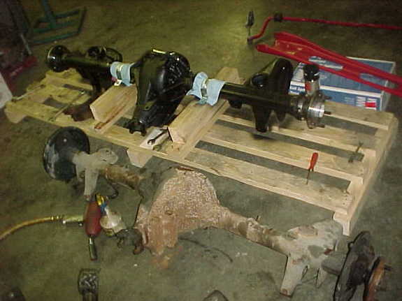 Refurbished black rear axle on wood pallets next to a rusty old axle on a garage floor