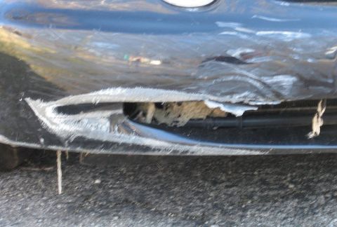 1999 Ford Taurus - The front bumper of a car has sustained significant damage, revealing underlying structures and torn material.