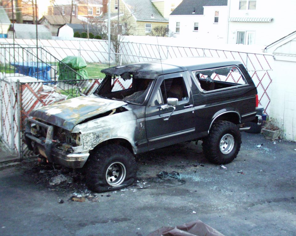 Burned black Ford Bronco with shattered windows and flat front tire, parked in a lot