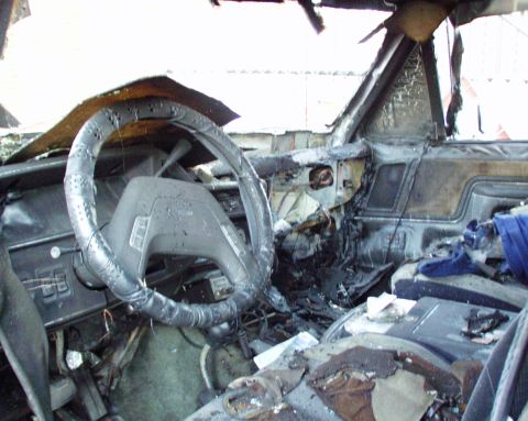 1989 Ford Bronco - The interior of a vehicle is heavily damaged by fire, with melted plastic and charred remnants visible.