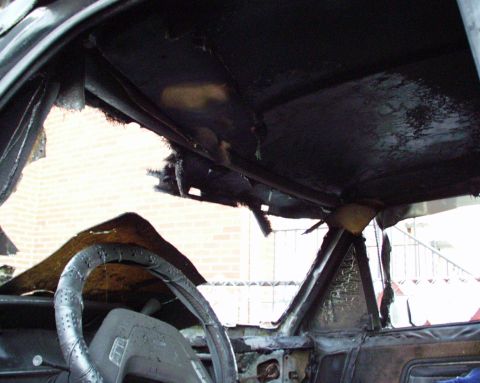 1989 Ford Bronco - The interior of a vehicle shows extensive fire damage, with the dashboard and steering wheel charred and torn.