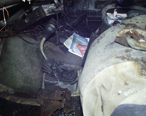 1989 Ford Bronco - The interior of a vehicle shows significant fire damage, with charred debris and melted components visible.