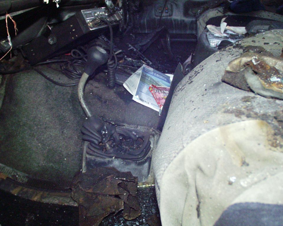 Interior of a burnt-out vehicle, showing a shifter, radio, and damaged seats
