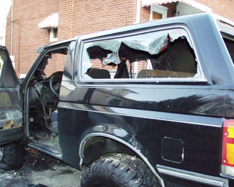 1989 Ford Bronco - This black 1989 Ford Bronco shows significant damage with broken windows and an open door, suggesting it has been through a difficult event.
