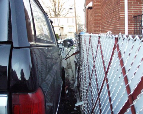 1989 Ford Bronco - A black SUV is parked very close to a chain-link fence, with a brick building visible in the background.