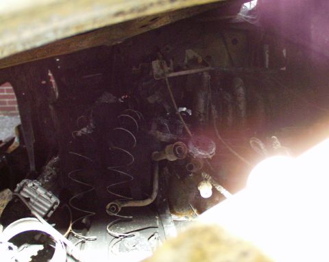 1989 Ford Bronco - The engine compartment of a vehicle is heavily damaged by fire, showing charred components and melted parts.